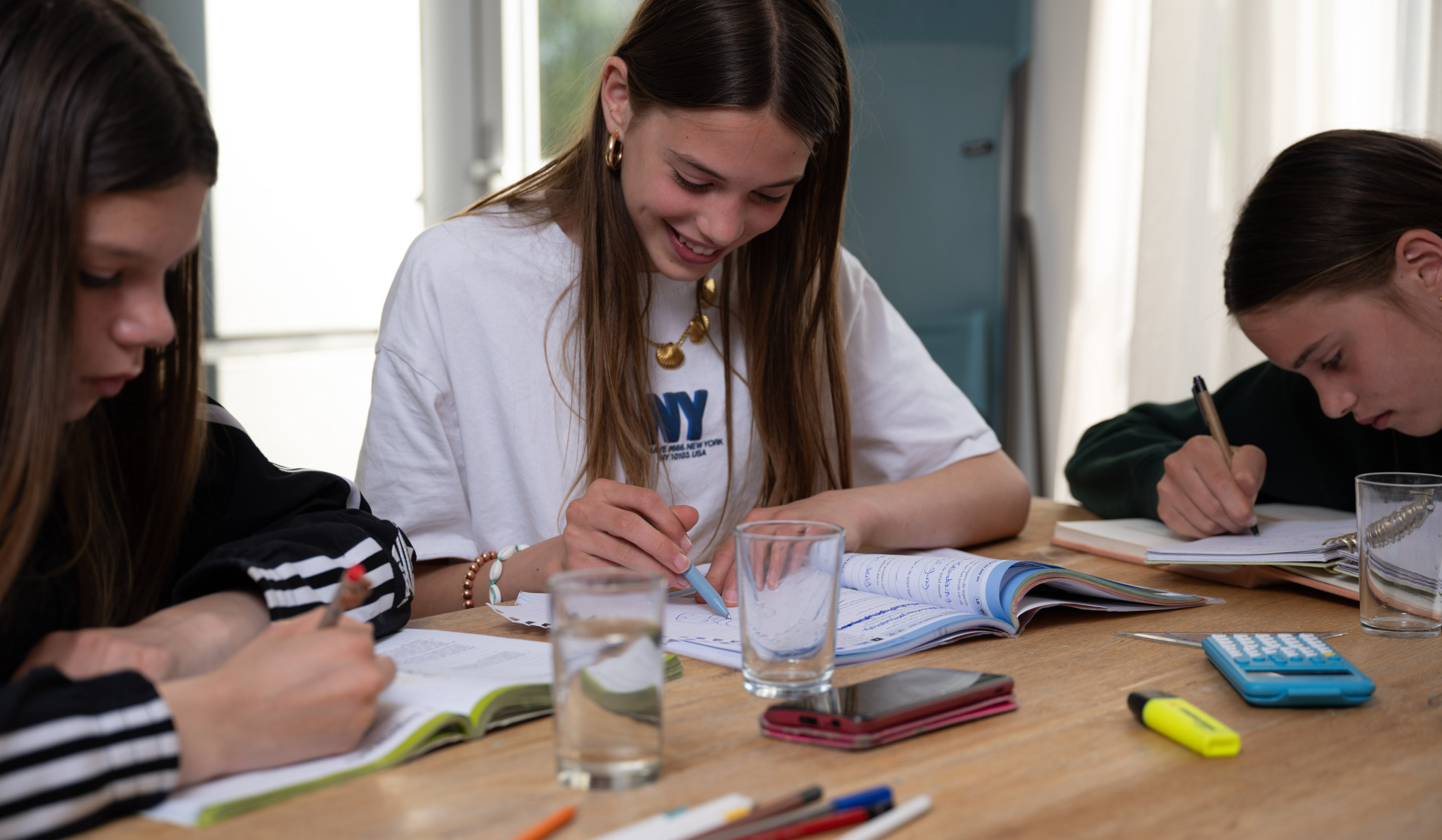 Drie jongeren maken huiswerk aan de keukentafel Drie jongeren maken huiswerk aan de keukentafel